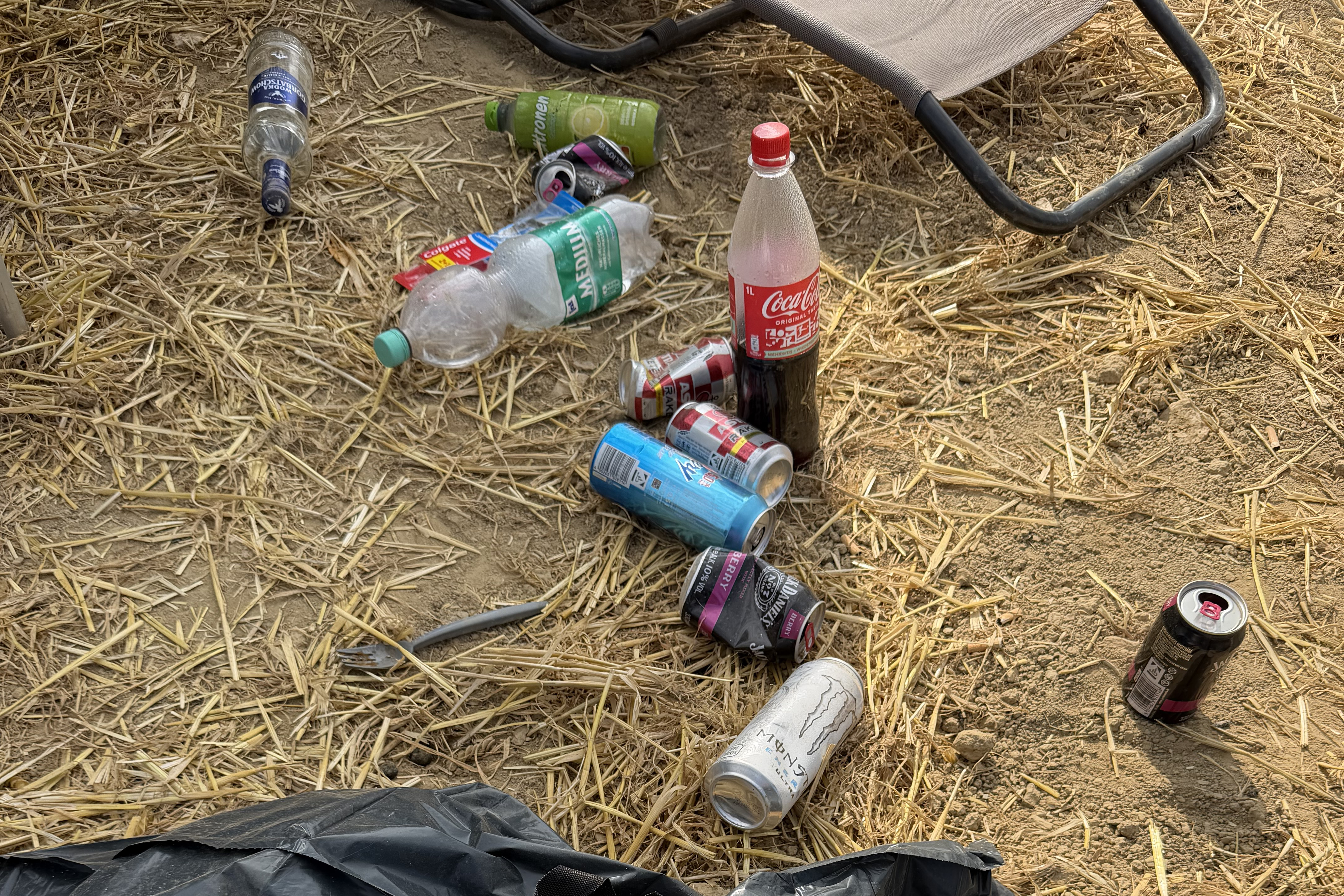 Leere Flaschen und Dosen liegen zwischen Stroh und trockenem Boden auf dem Campingplatz.