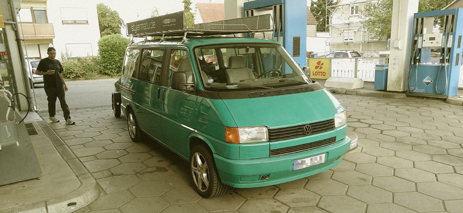 Analoge Film-Fotografie eines türkisfarbenen VW T4 Transporters an einer Aral-Tankstelle beim Roadtrip.