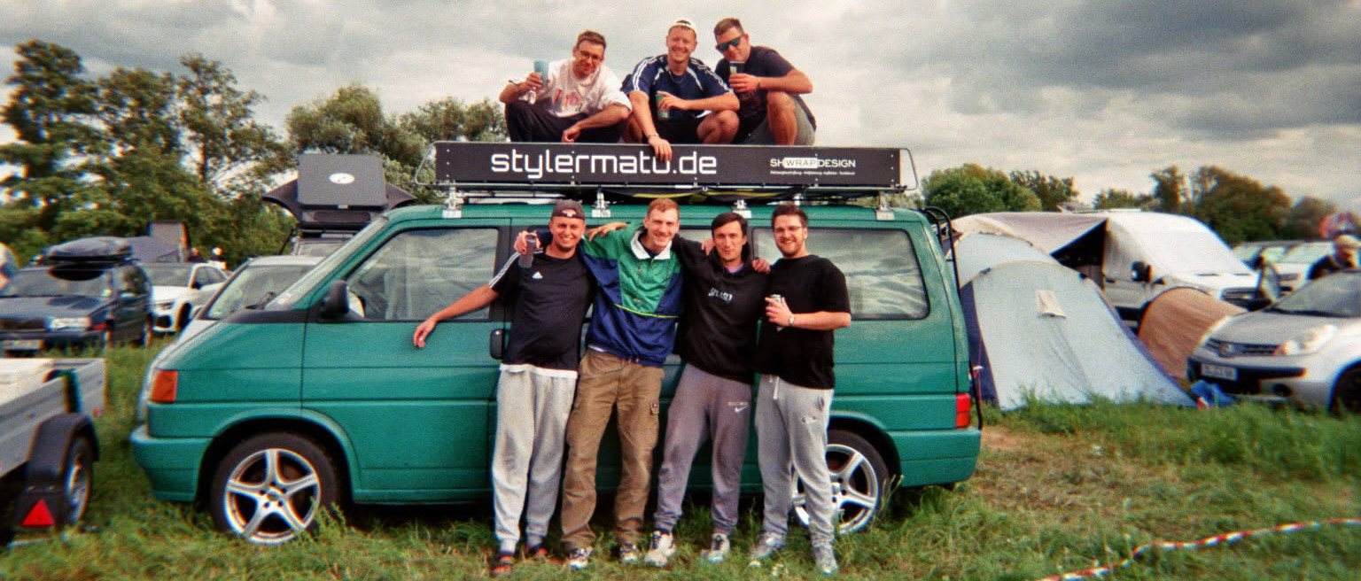 Sieben Freunde posieren beim splash! Festival 2026 vor einem grünen VW-Bus mit stylermatu.de-Banner auf dem Campingplatz.
