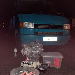 Transporter bei Nacht auf einem Parkplatz, davor Müll, Getränkeflaschen und ein improvisierter Aufbau.