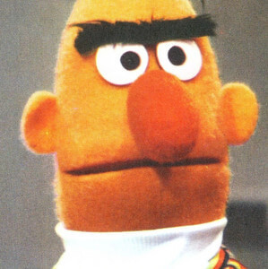 Nahaufnahme der Figur Ernie mit ernstem Gesichtsausdruck vor neutralem Hintergrund.