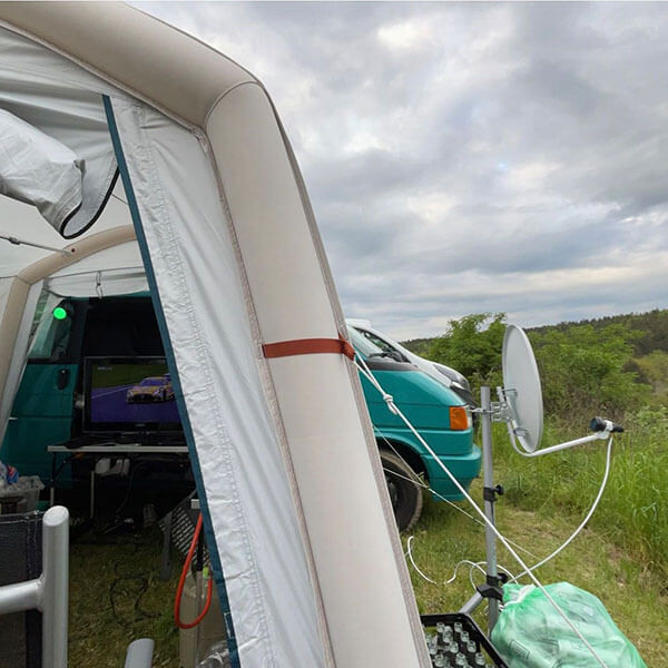 Provisorischer Outdoor-Aufbau mit Fahrzeug, Technik und Satellitenschüssel auf einer Wiese.