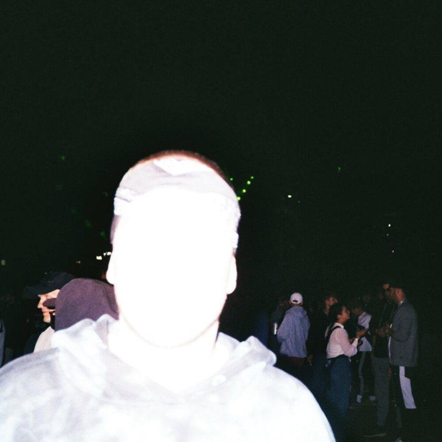 Überbelichtete Person im Vordergrund bei Nacht, Gesicht kaum erkennbar; im Hintergrund eine Menschenmenge.